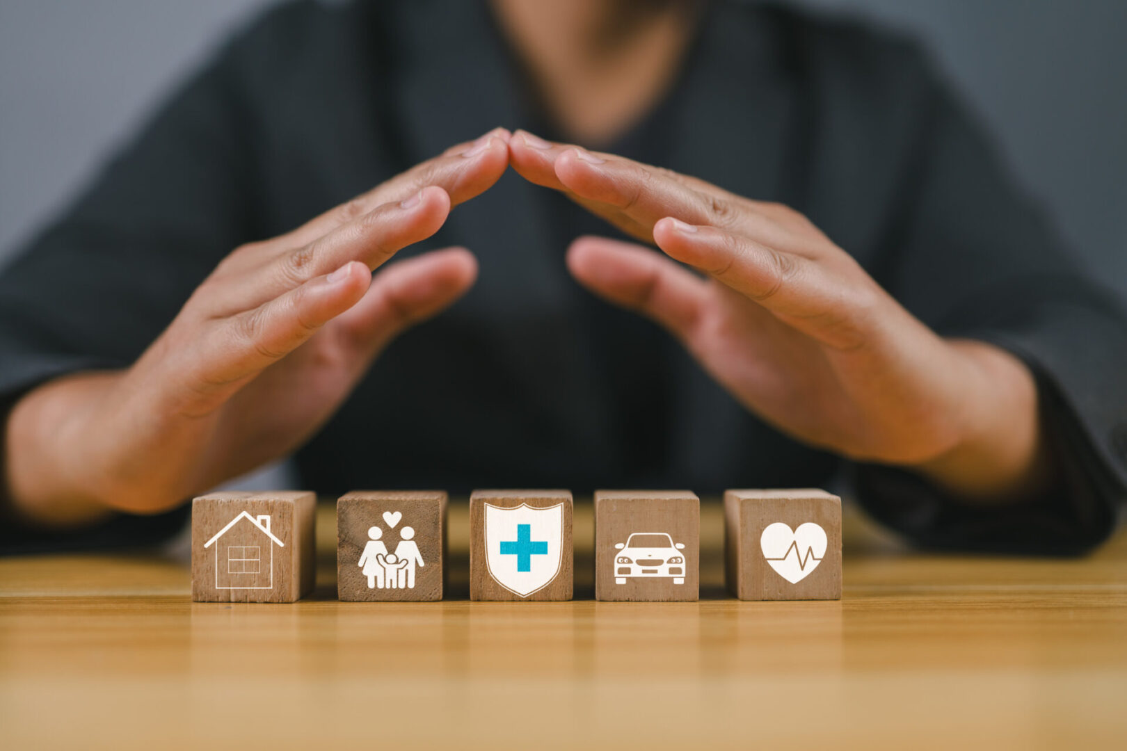 Hands protecting insurance-related wooden blocks.