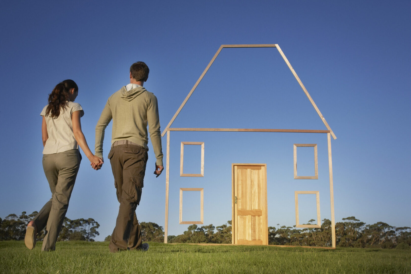 Couple walking towards wooden house outline.